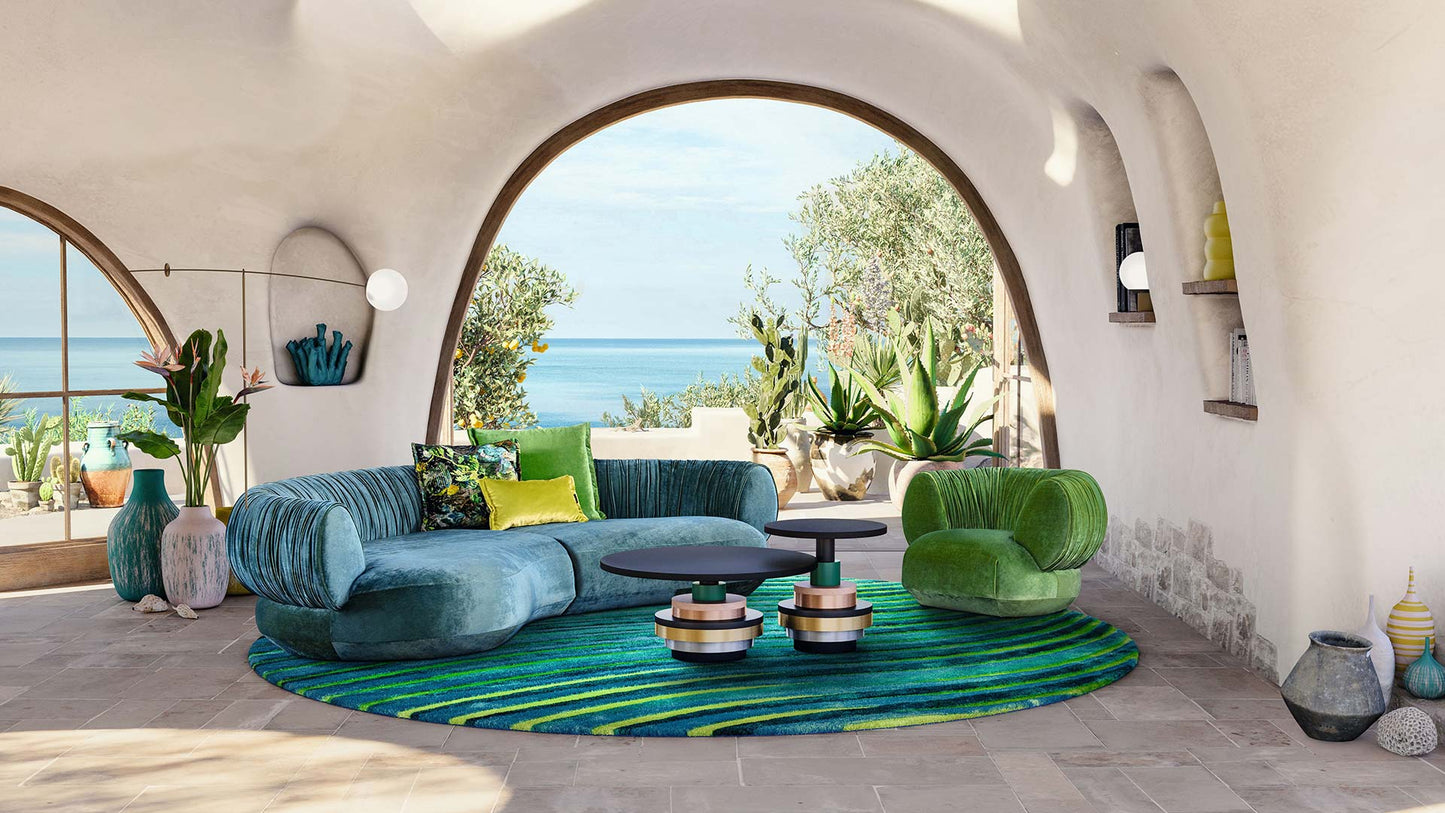 Bretz Couch Nanami aus blauem Velours in einem gewölbtem Raum mit Ausblick auf das Meer.