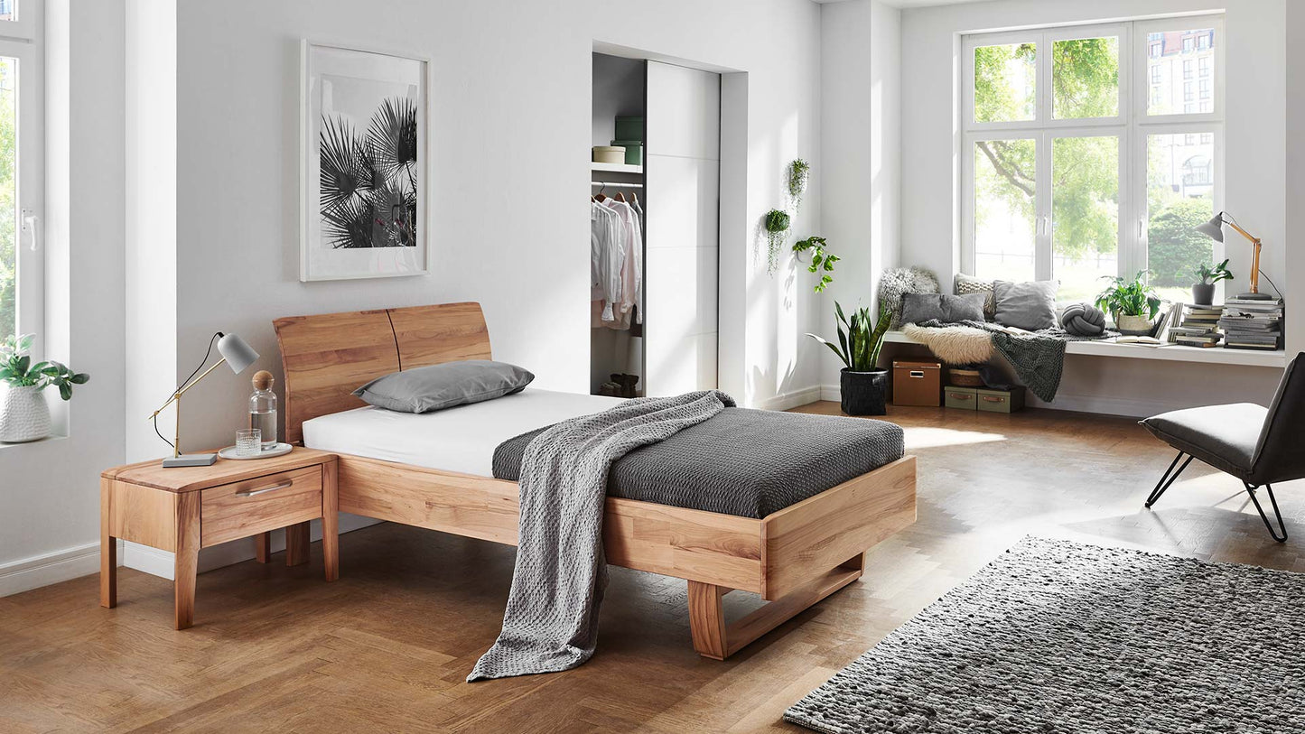 Helles Schlafzimmer mit Holzbett aus Eiche oder Kernbuche mit Kufe und Nachttisch aus Massivholz.