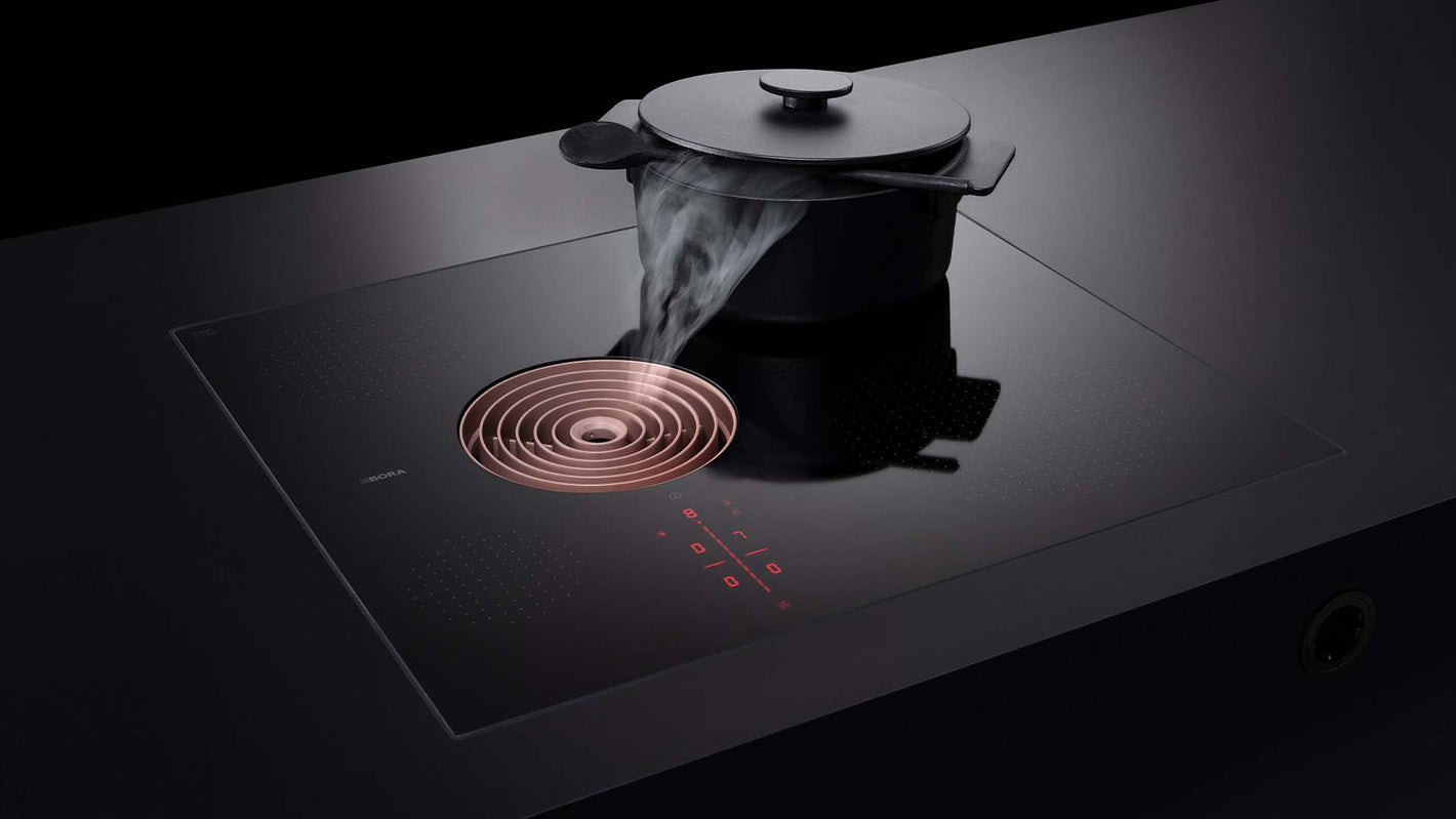 Schwarzer Küchenblock mit BORA Kochfeld mit Dunstabzug mit kupferfarbener Einströmdüse.