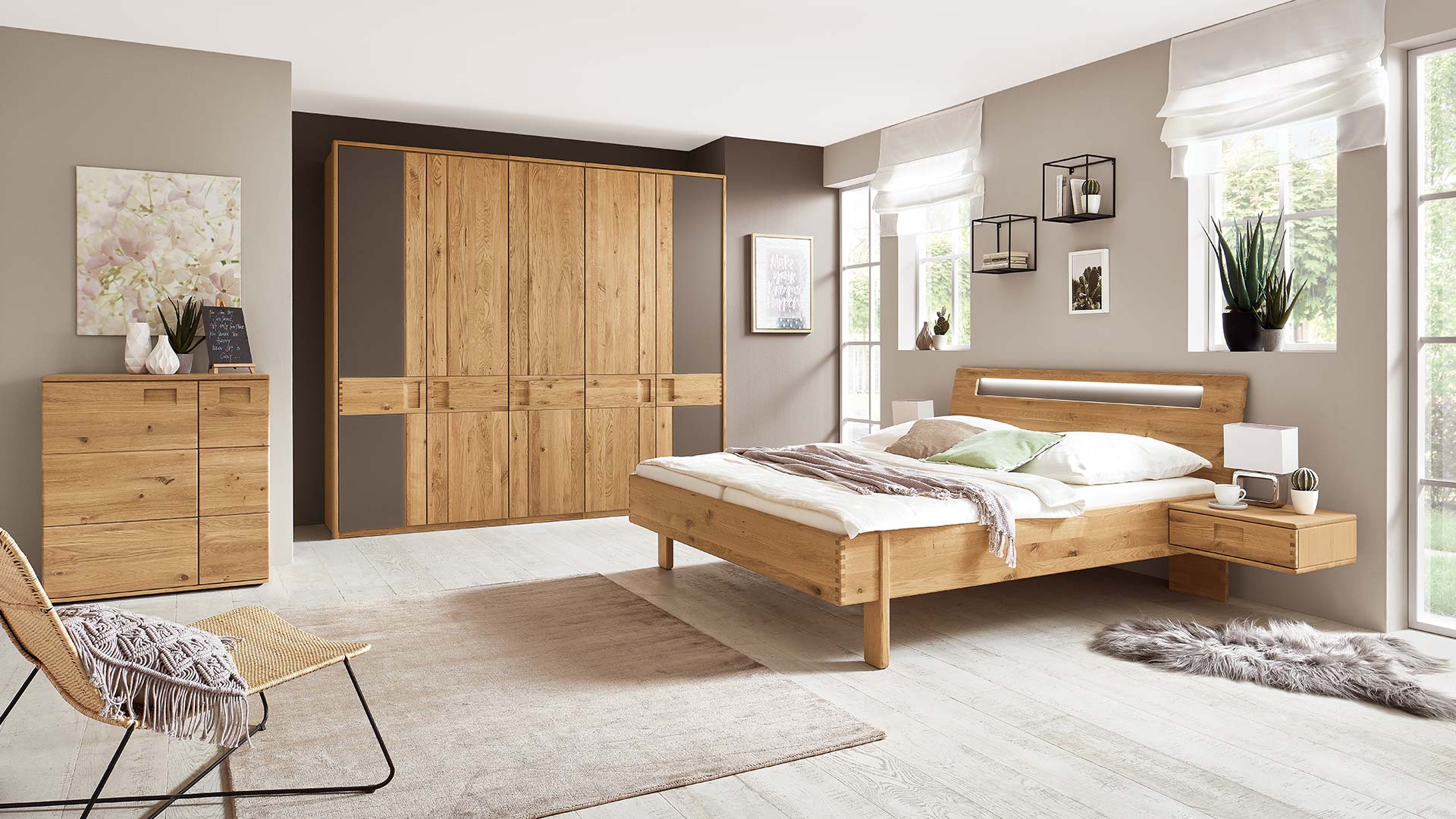 Schlafzimmersystem in einem beigen Schlafzimmer mit Massivholzbett in Eiche oder Buche mit Nachtkonsole, Kleiderschrank und Kommode.
