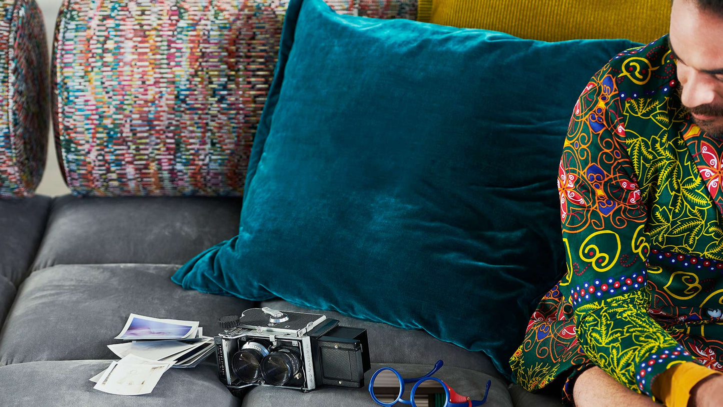 Ed Couch von Bretz silbernem Velours und bunt gemusterten Polsterrollen und blauem und gelbem Plaidkissen in Velours und Cord.