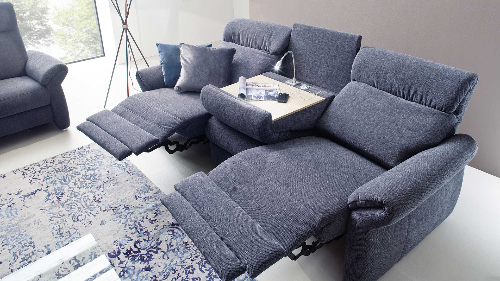 Sofa mit Relaxfunktion, elektrisch verstellbare Fußstützen und Rückenlehnen, dunkelblauer Stoffbezug und Mitteltisch mit Leselampe und USB Anschlüssen