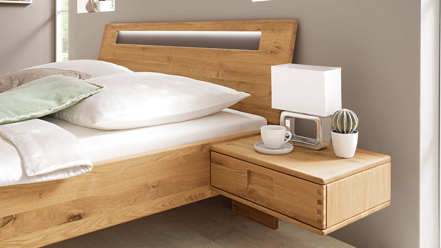  Schlafzimmersystem in einem beigen Schlafzimmer mit Massivholzbett in Eiche oder Buche mit Nachtkonsole, Kleiderschrank und Kommode.
