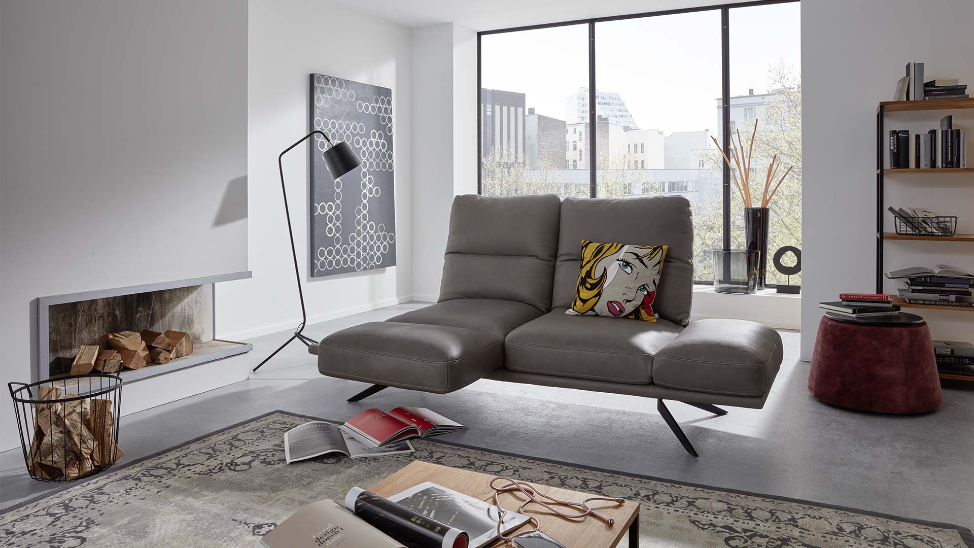 Heller Raum mit einem Funktionssofa aus Leder in grau mit Metallfüßen und drehbarem Sitzkissen.