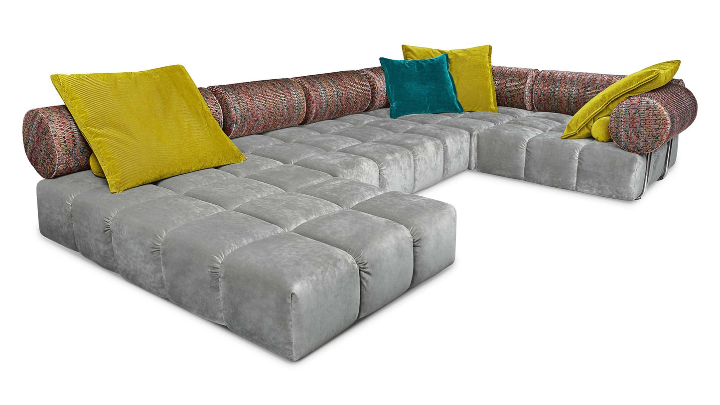 Ed Couch von Bretz silbernem Velours ohne Füße und bunt gemusterten Polsterrollen und blauem und gelbem Plaidkissen in Velours und Cord.