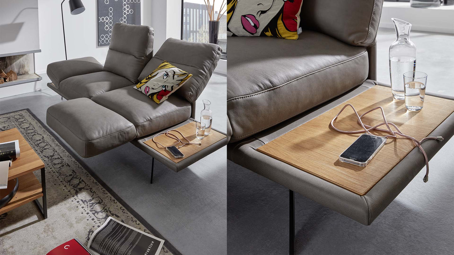 Funktionssofa aus Leder in grau mit klappbarer Armlehne und drehbarem Sitzkissen zu einem Tisch aus Holz.