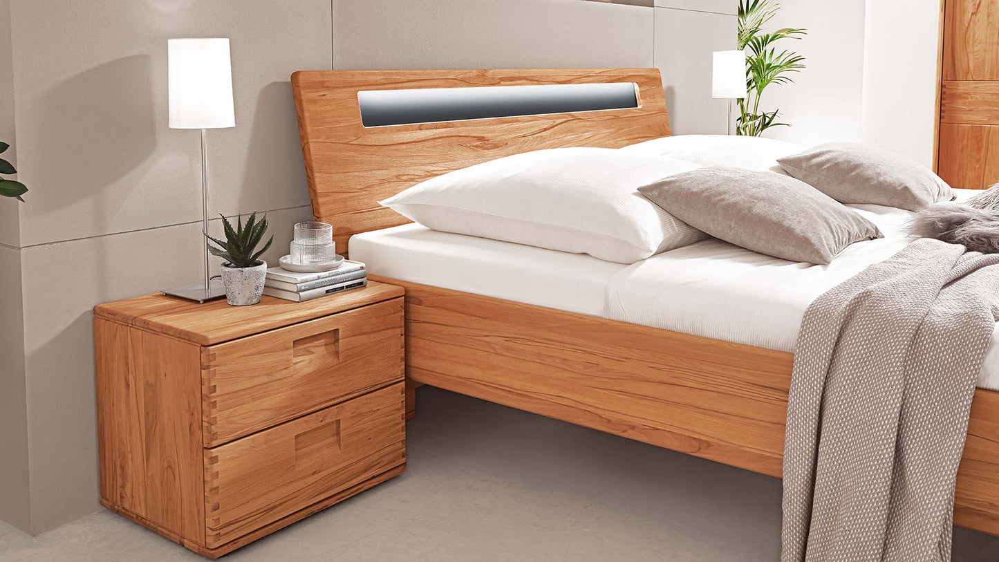 Schlafzimmersystem in einem beigen Schlafzimmer mit Massivholzbett in Eiche oder Buche mit Nachttisch, Kleiderschrank und Kommode und Garderobe mit Spiegel.