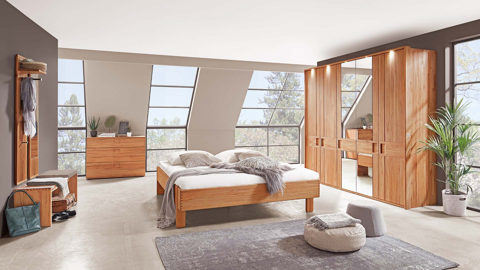 Schlafzimmersystem in einem beigen Schlafzimmer mit Massivholzbett in Eiche oder Buche mit Nachttisch, Kleiderschrank mit Spiegel und Kommode und Garderobe mit Spiegel.