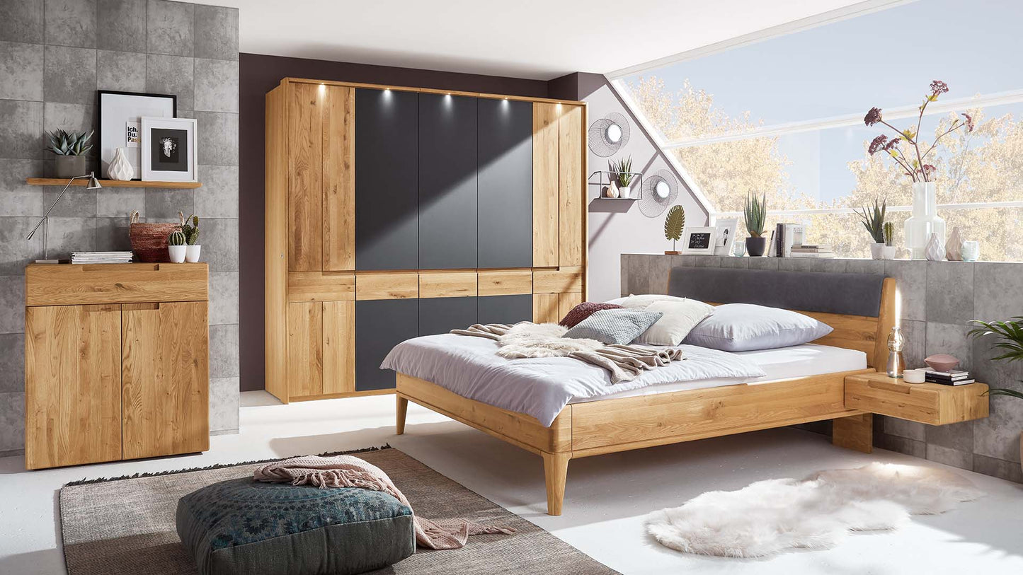 Schlafzimmersystem aus Massivholz Wildeiche mit Naturholzbett beleuchtet mit Lederrückenteil, schwebender Nachtkonsole, Kleiderschrank beleuchtet mit schwarzen Fronten und Kommodenschrank.