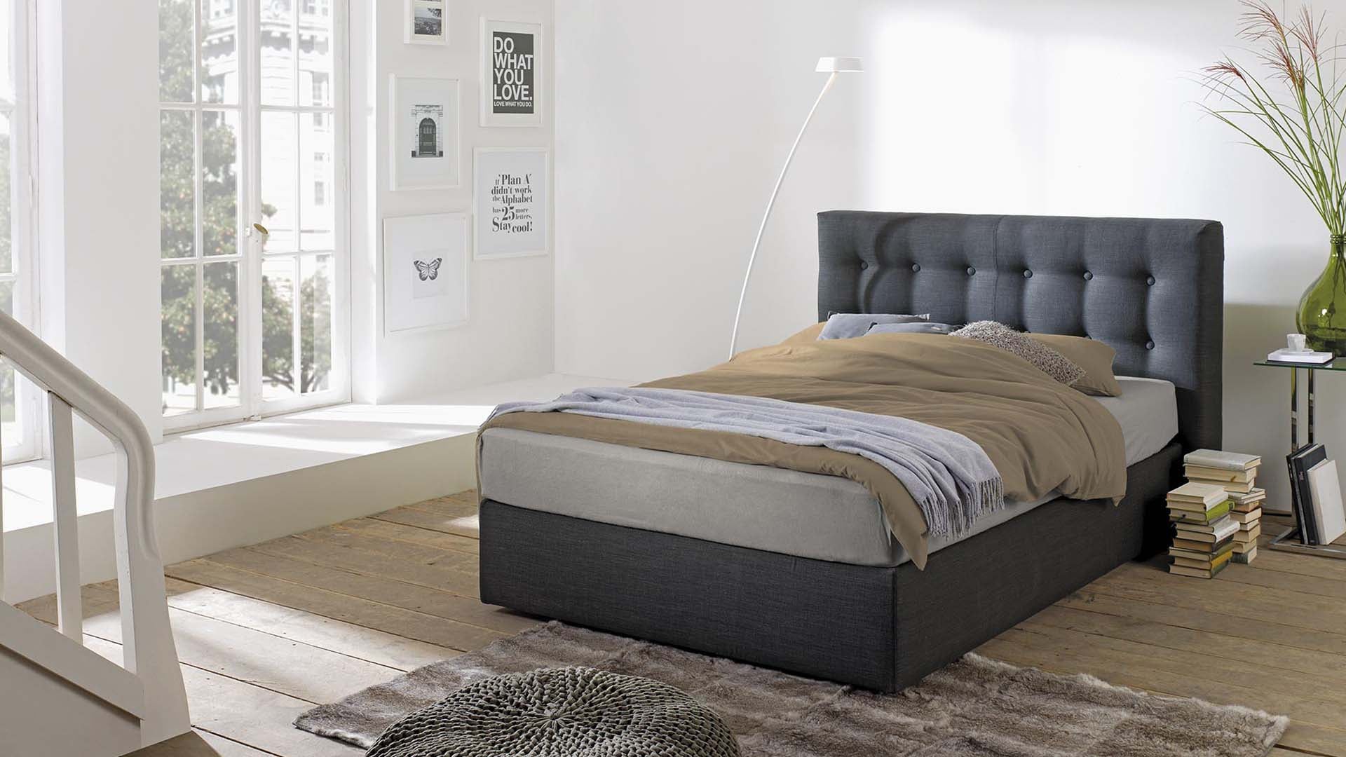 Helles Schlafzimmer mit Hüsler Nest Bett in anthrazitfarbenem Stoff und Knopfoptik-Kopfteil als natürliches Boxpsringbett.