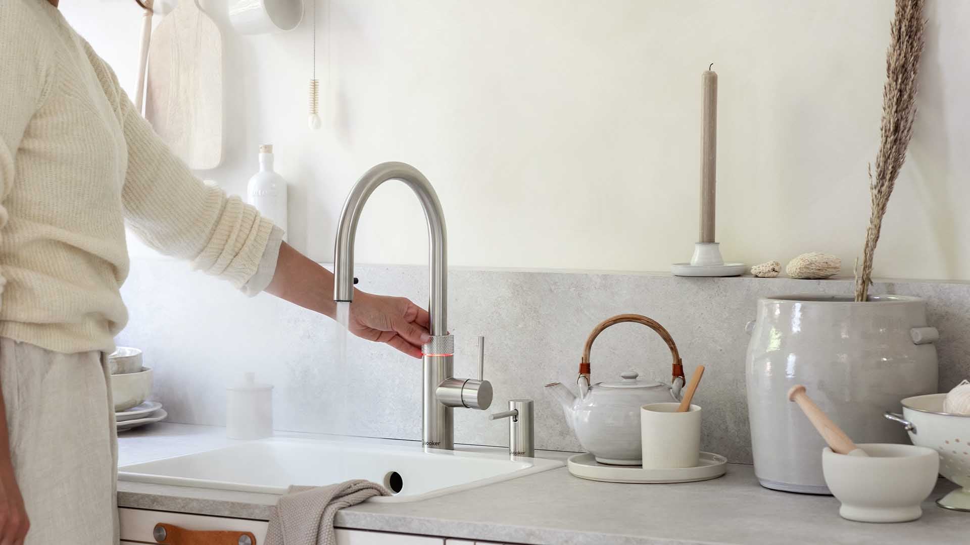 Helle Küchenzeile mit Spüle und dem Quooker Flex Wasserhahn aus Edelstahl, von welchem Heißwasser runtergelassen wird.