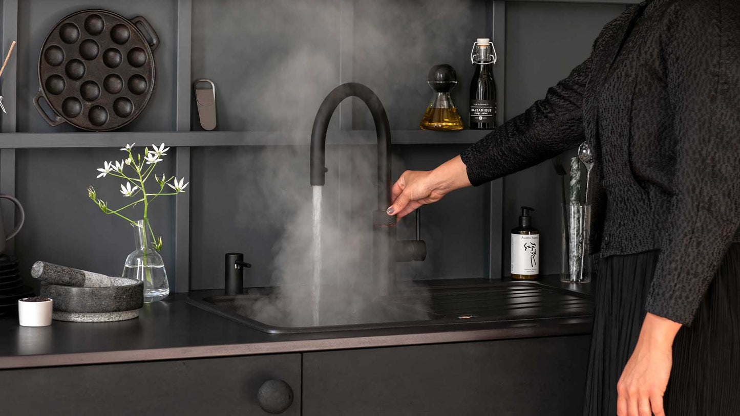 Dunkle Küchenzeile mit Spüle und dem Quooker Flex Wasserhahn in schwarz, von welchem Heißwasser runtergelassen wird.